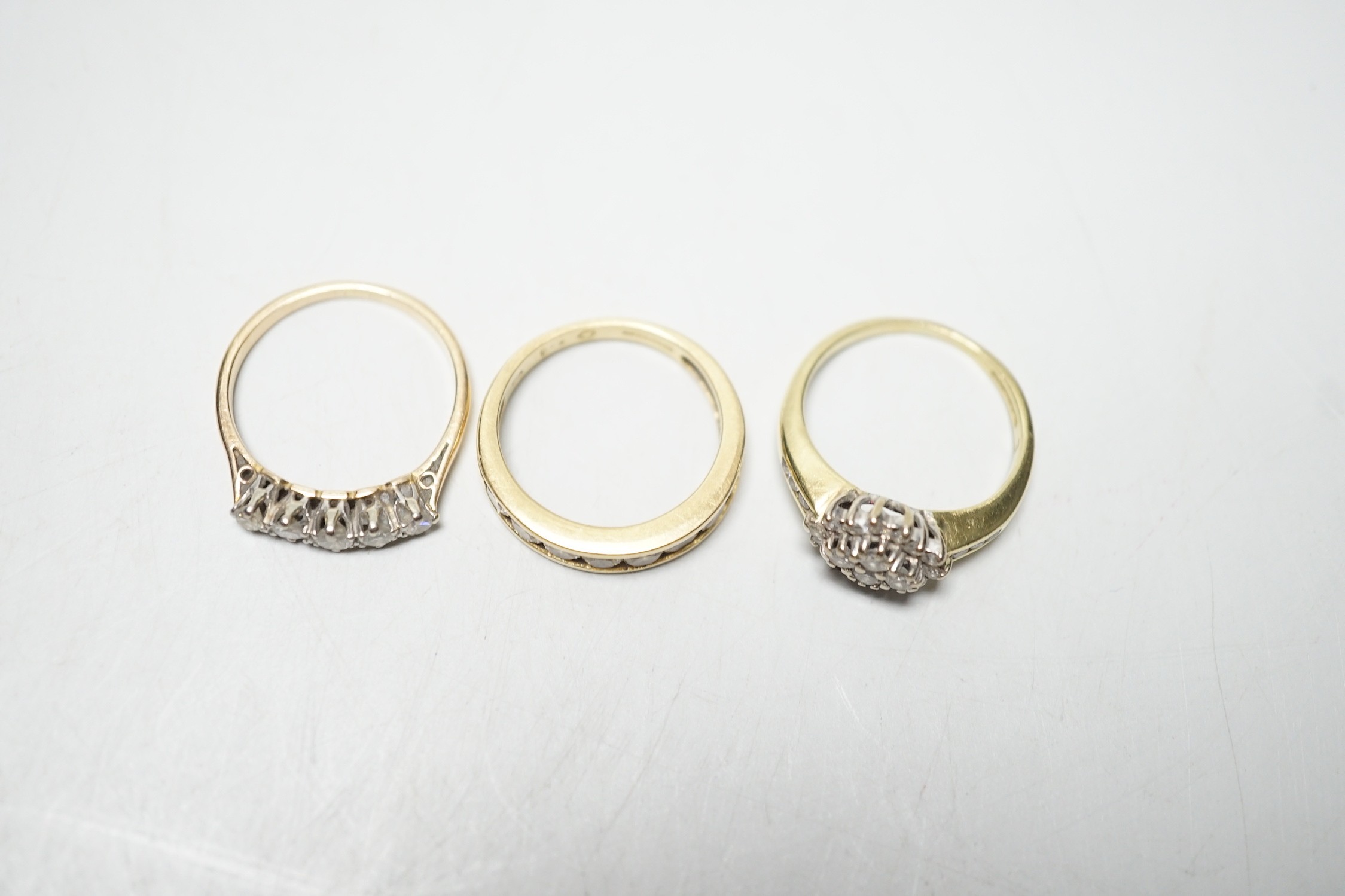 Two modern 18ct gold and diamond set rings, including nine stone channel set, size L and diamond cluster, size L and a yellow metal and five stone diamond set half hoop ring, size M, gross weight 9 grams.